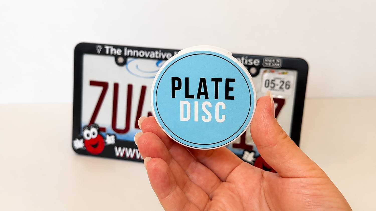 A Plate Disc held in hand in front of a Plate Disc license plate frame